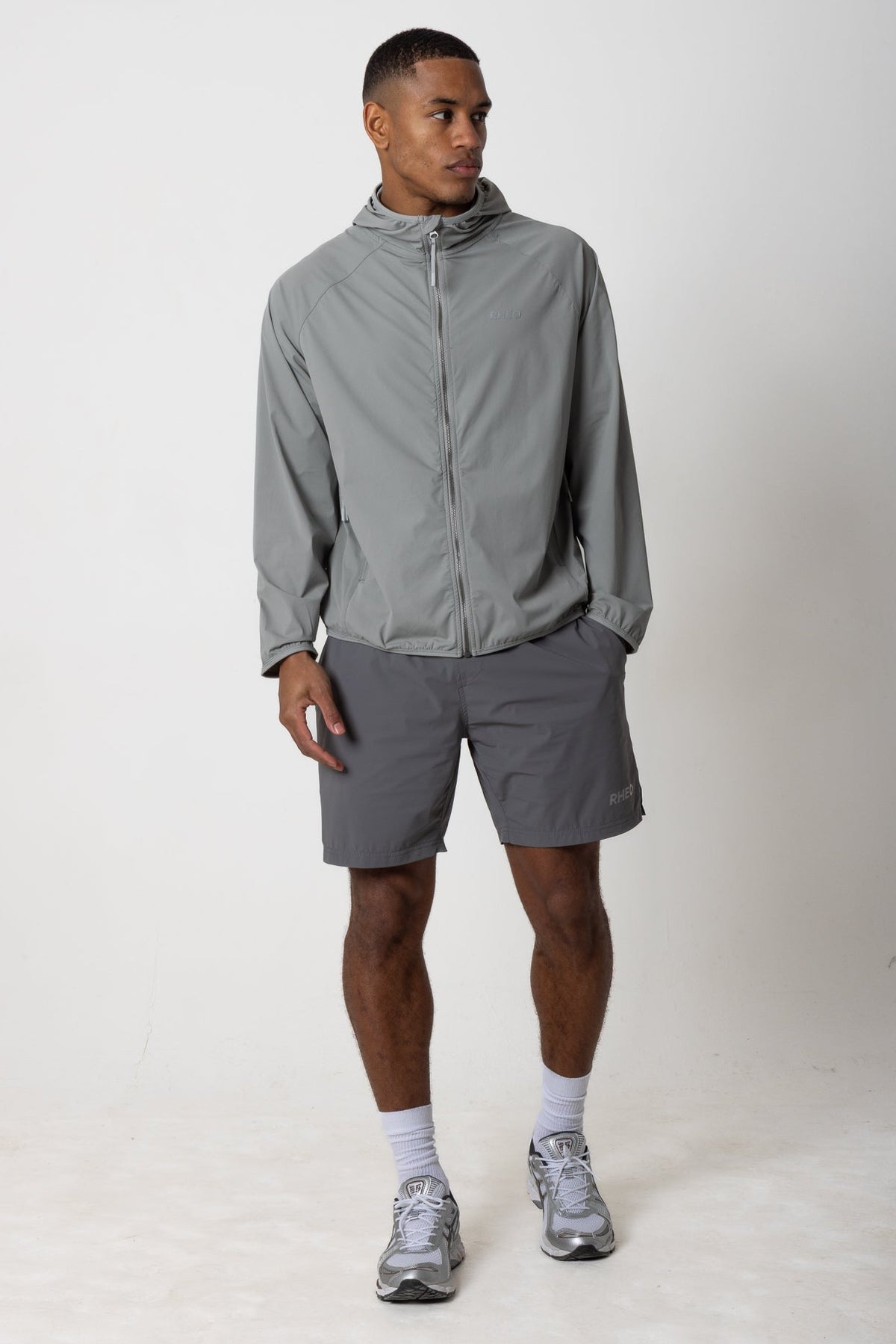 Man wearing the grey RHEO PebbleShell™ Windbreaker with grey shorts, showing the front fit and hood.