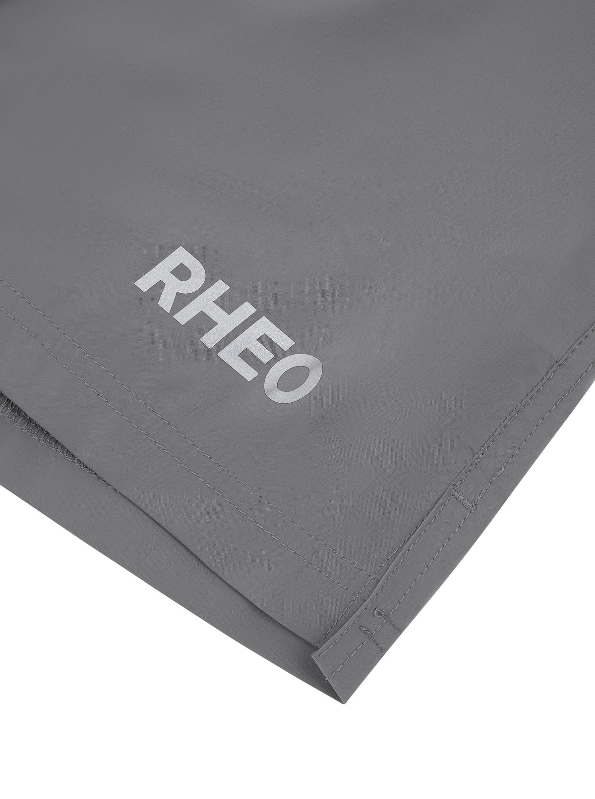 Close-up of grey RHEO ClayShell™ 7" Shorts showing the RHEO logo and stitched hem.
