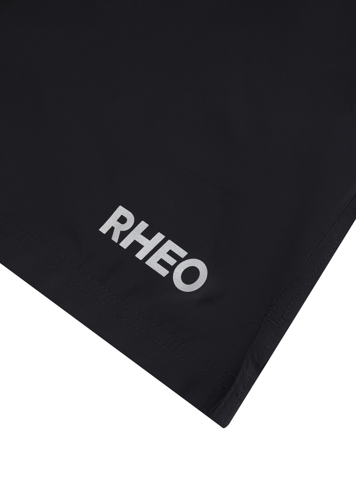 Close-up of black RHEO ClayShell™ 7" Shorts showing the textured fabric, RHEO logo and stitched hem.