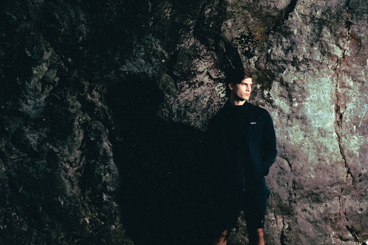 Athlete in the PebbleShell windbreaker against a dark gritstone wall