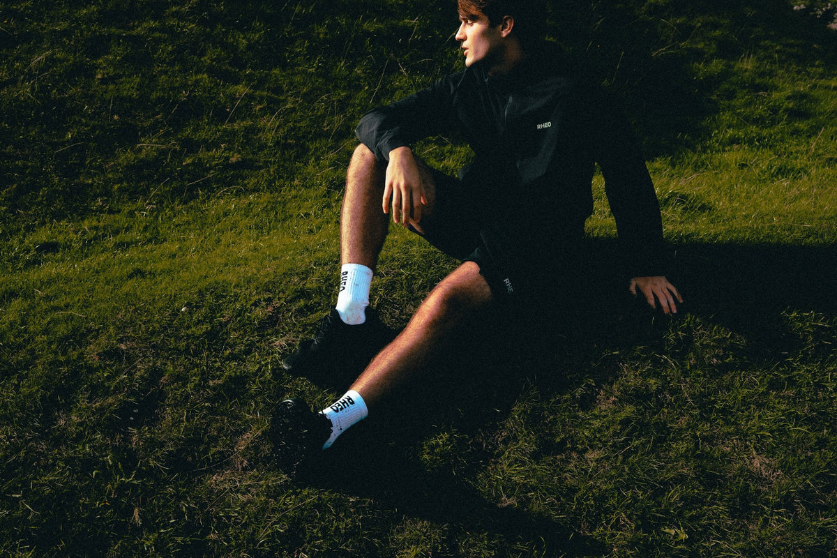 Athlete resting on a sunlit Peak District hillside in RHEO kit