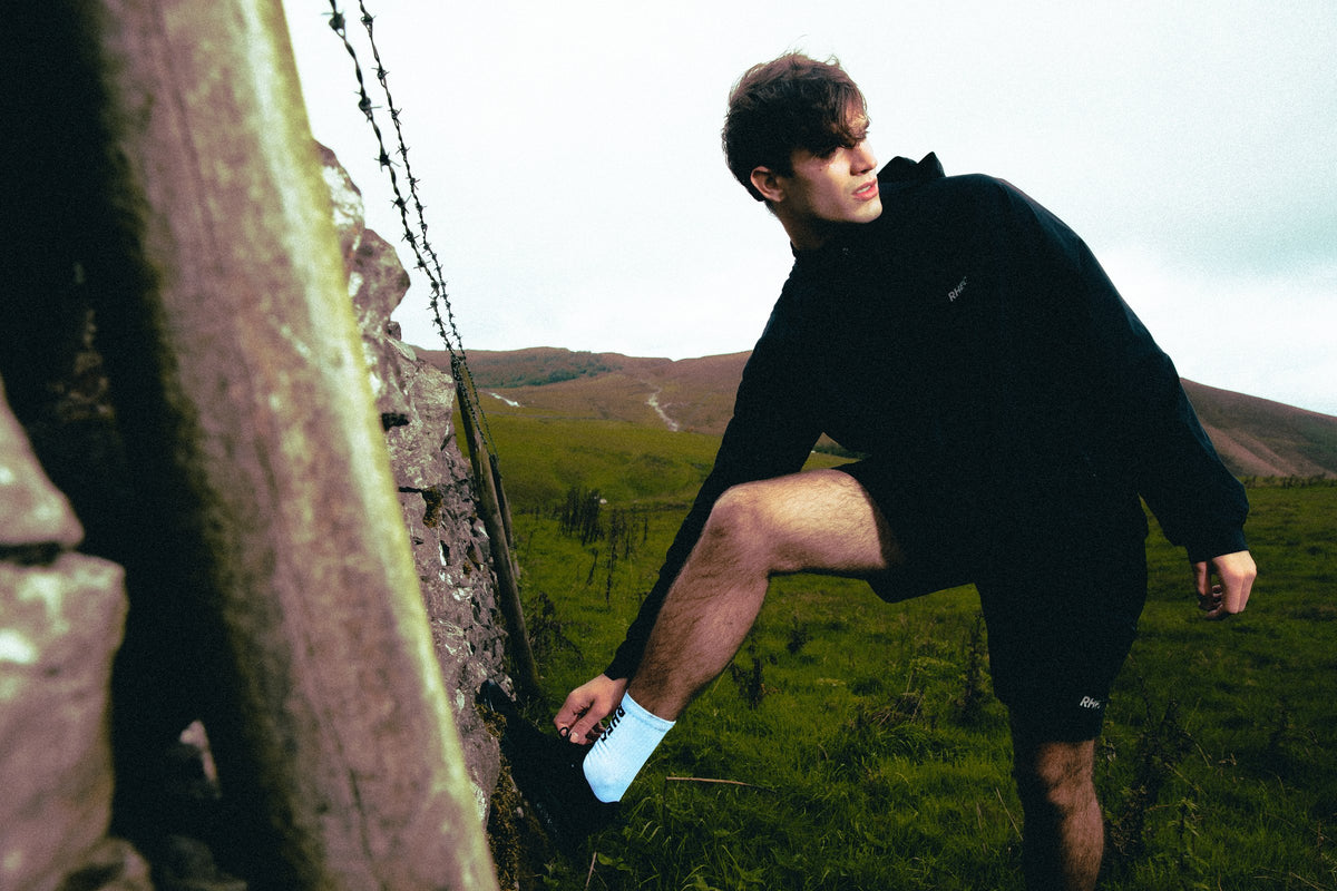 Athlete in a hooded black RHEO top climbing a dry-stone wall in the Peak District